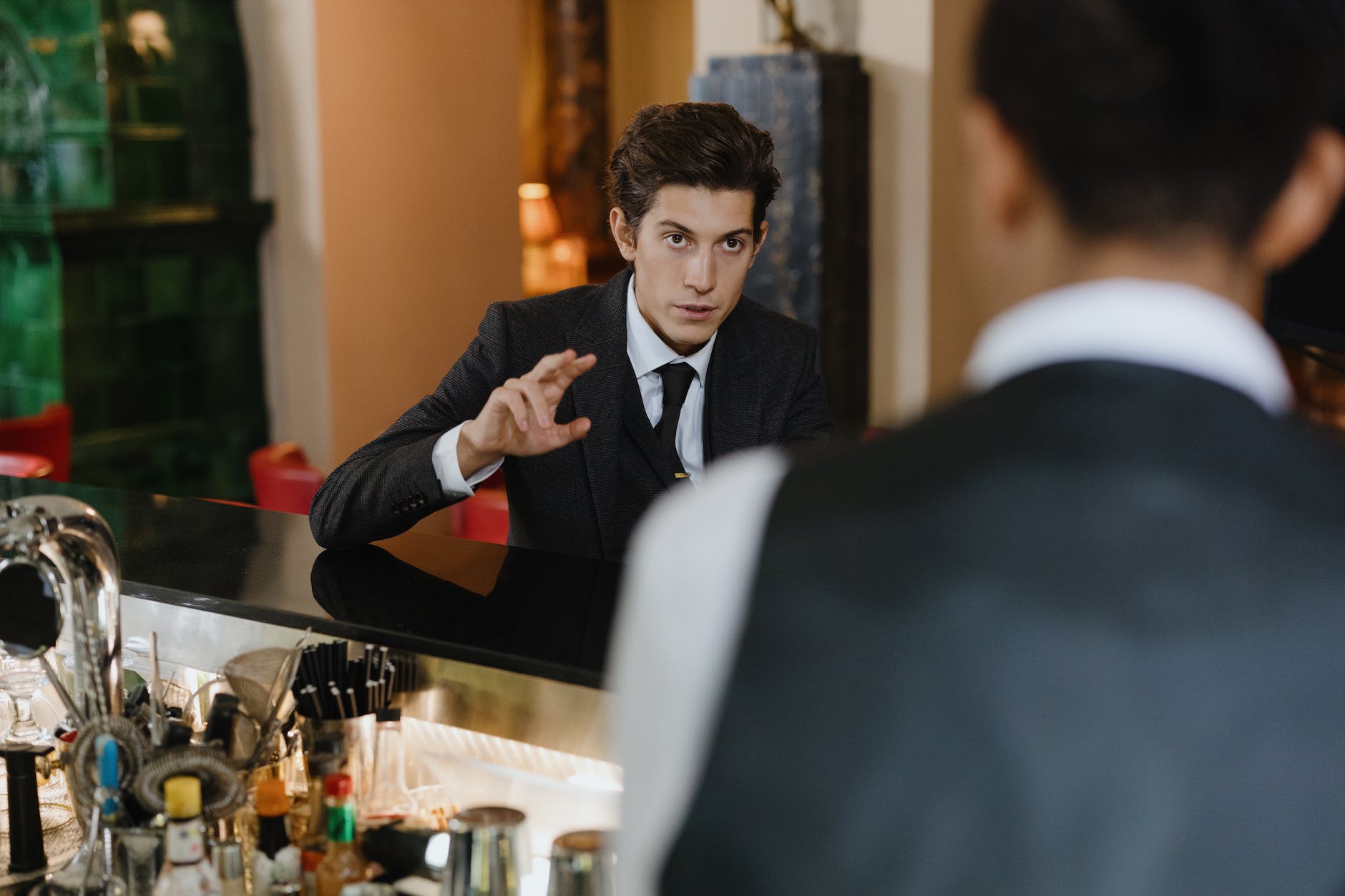 man in black suit talking to a man in front