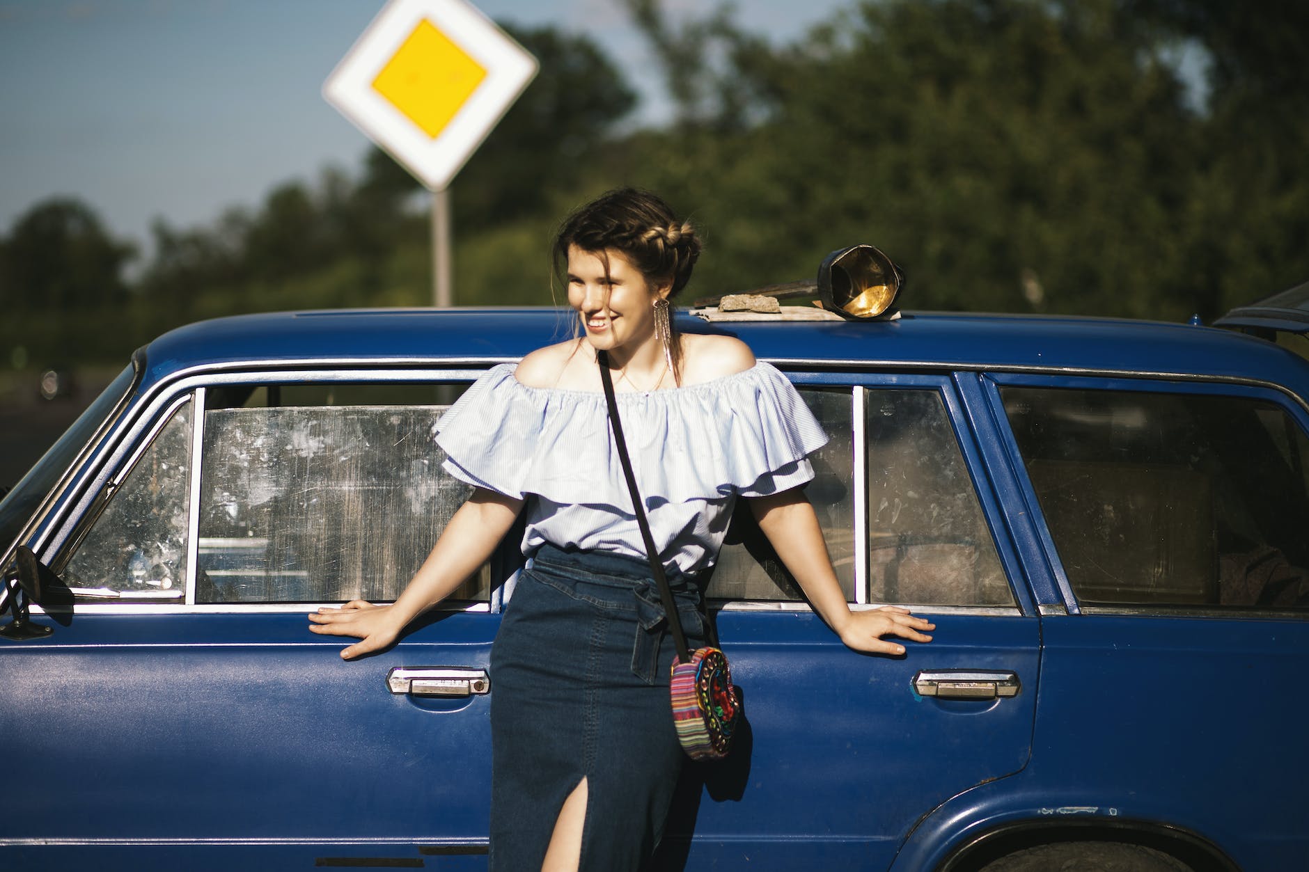 woman wearing white off shoulder top while touching blue car
