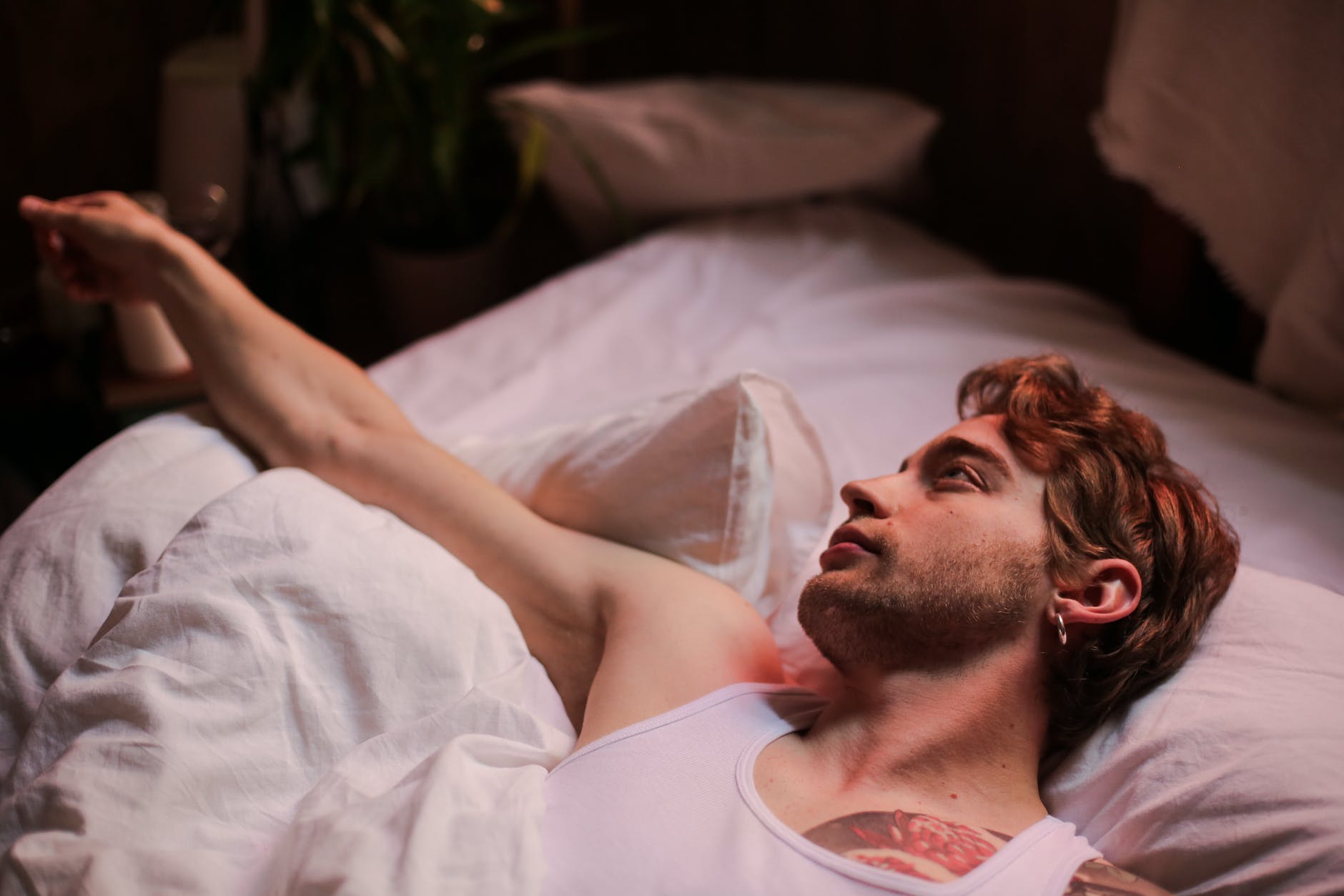 man in white tank top lying on bed